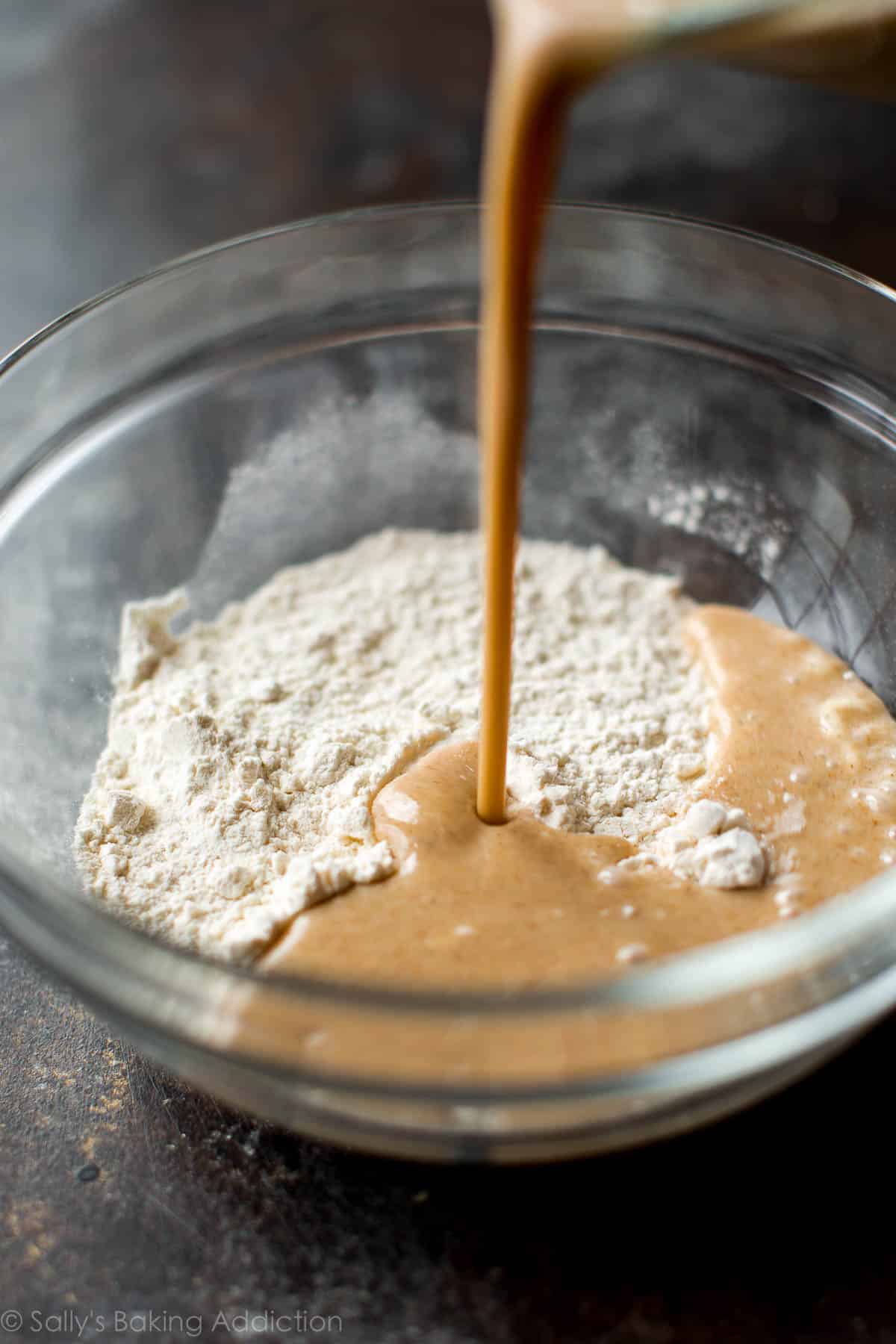 pouring wet ingredients into a glass bowl with dry ingredients