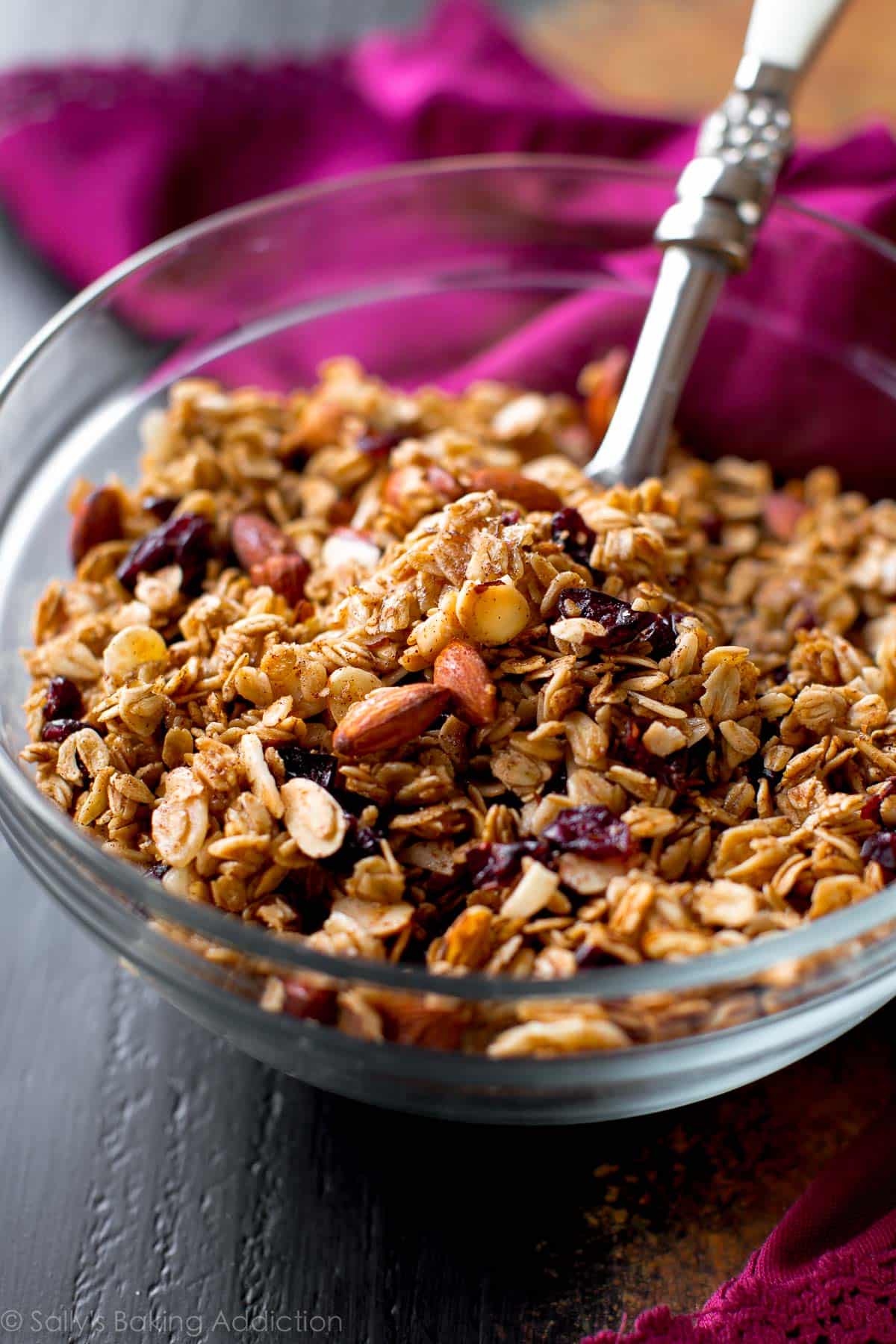 maple almond cranberry granola in a glass bowl with a serving spoon