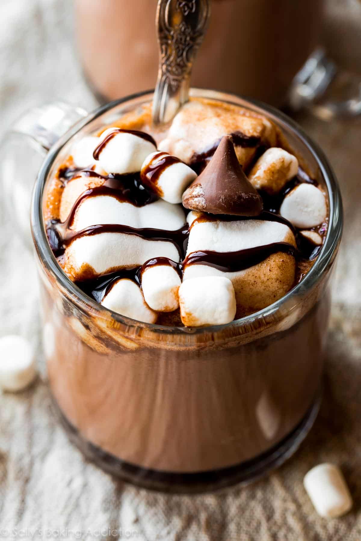 glass mug of hot chocolate topped with marshmallows, chocolate sauce, and a Hershey's kiss