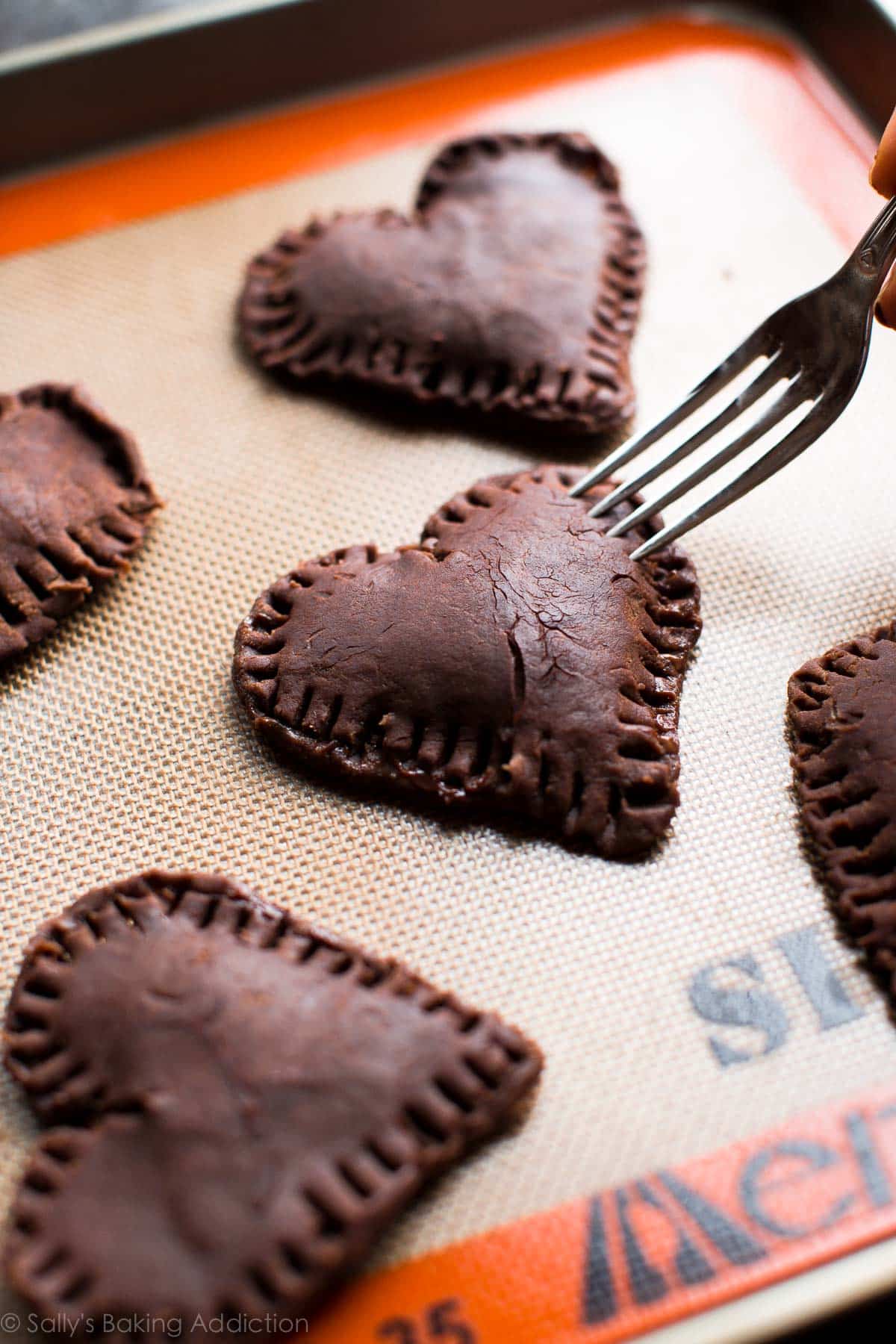 using a fork to seal the chocolate hand pies shut on a silpat baking mat on a baking sheet