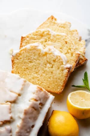 iced lemon pound cake loaf slices on marble board with lemons on the side.