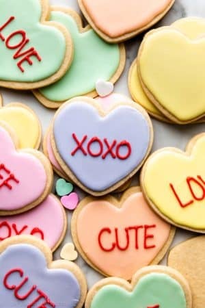 heart-shaped Valentine's Day cookies decorated in pastel royal icing and red writing to look like conversation heart candies.