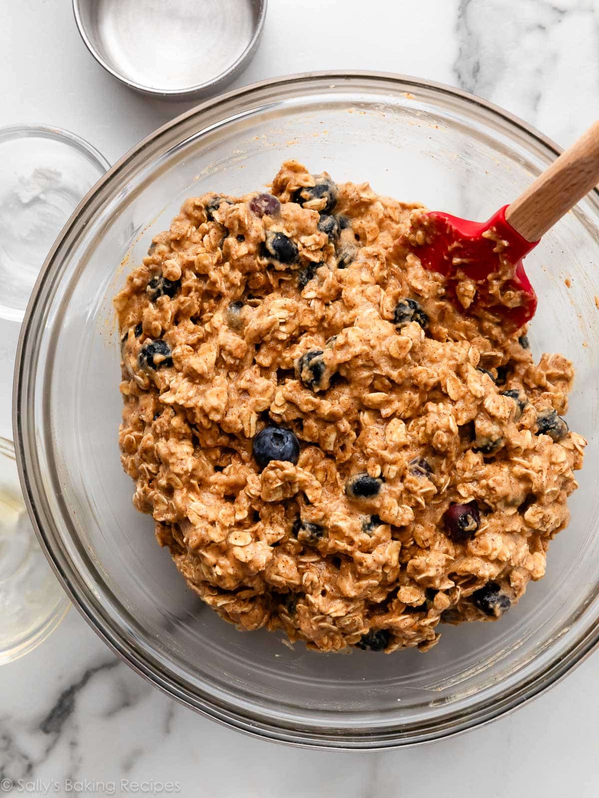 oatmeal almond blueberry batter in glass bowl with red spatula.