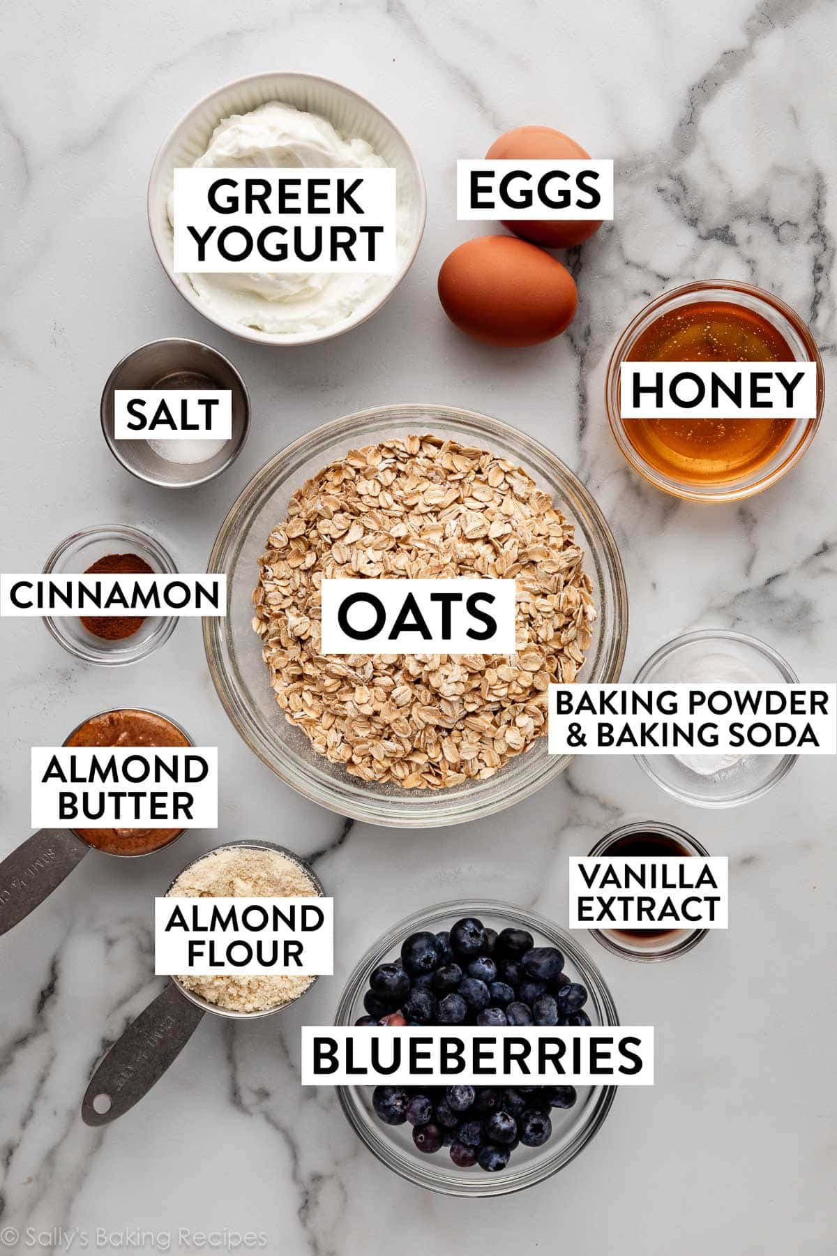 ingredients measured in bowls on counter including greek yogurt, oats, almond flour, almond butter, honey, and cinnamon.