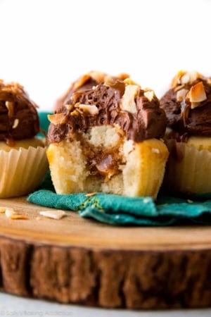 chocolate caramel coconut cupcakes on a wood slice serving board with a bite out of one showing the caramel filling