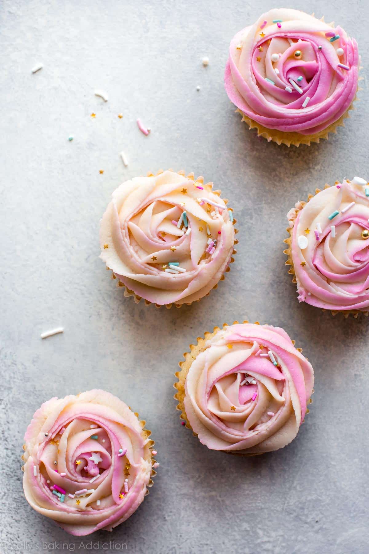 overhead image of cupcakes with pink frosting roses on top with sprinkles