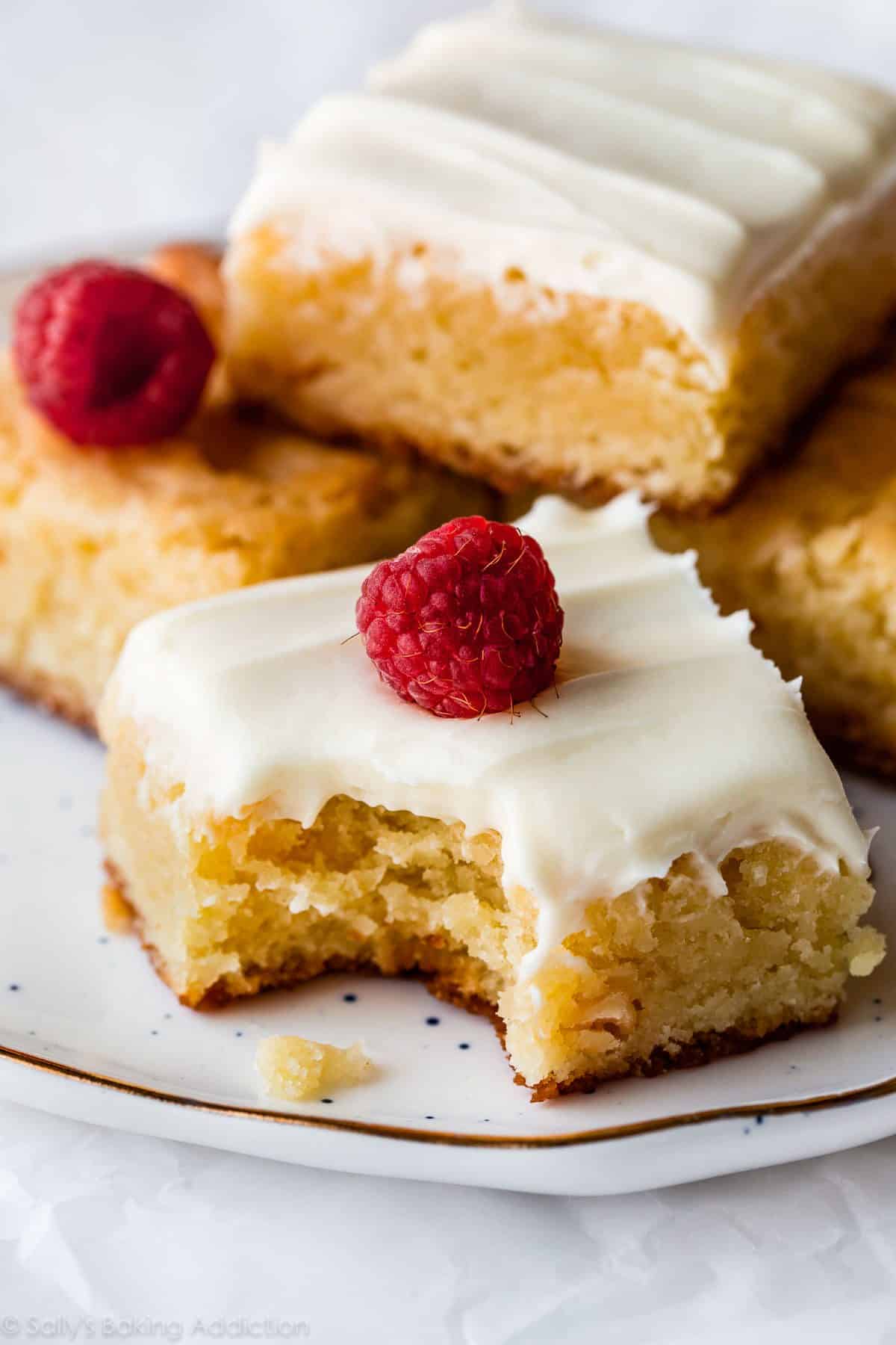 white chocolate brownies on a white plate topped with frosting and raspberries