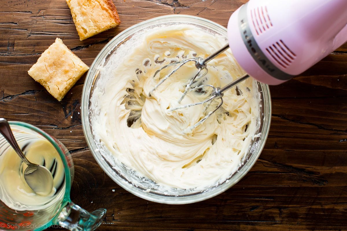 overhead image of white chocolate cream cheese frosting in a glass bowl with a hand mixer