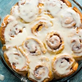 overhead image of orange sweet rolls with orange icing in a glass baking dish