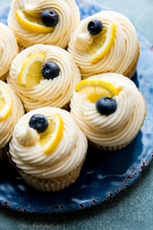 cupcakes with lemon buttercream frosting topped with blueberries and lemon slices on a blue plate