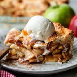 apple pie slice on plate with melty vanilla ice cream scoop on top.