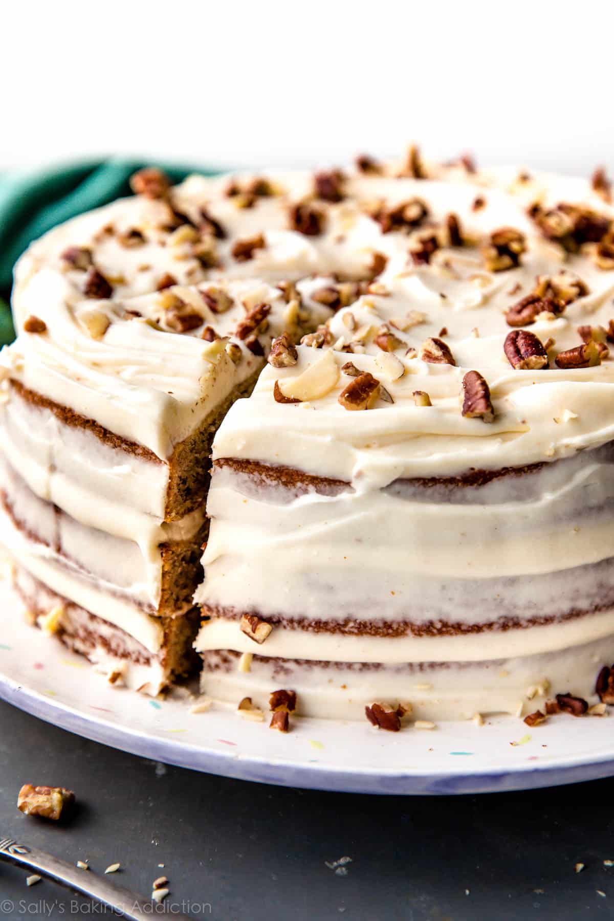 banana layer cake on a plate with brown butter cream cheese frosting and chopped pecans on top