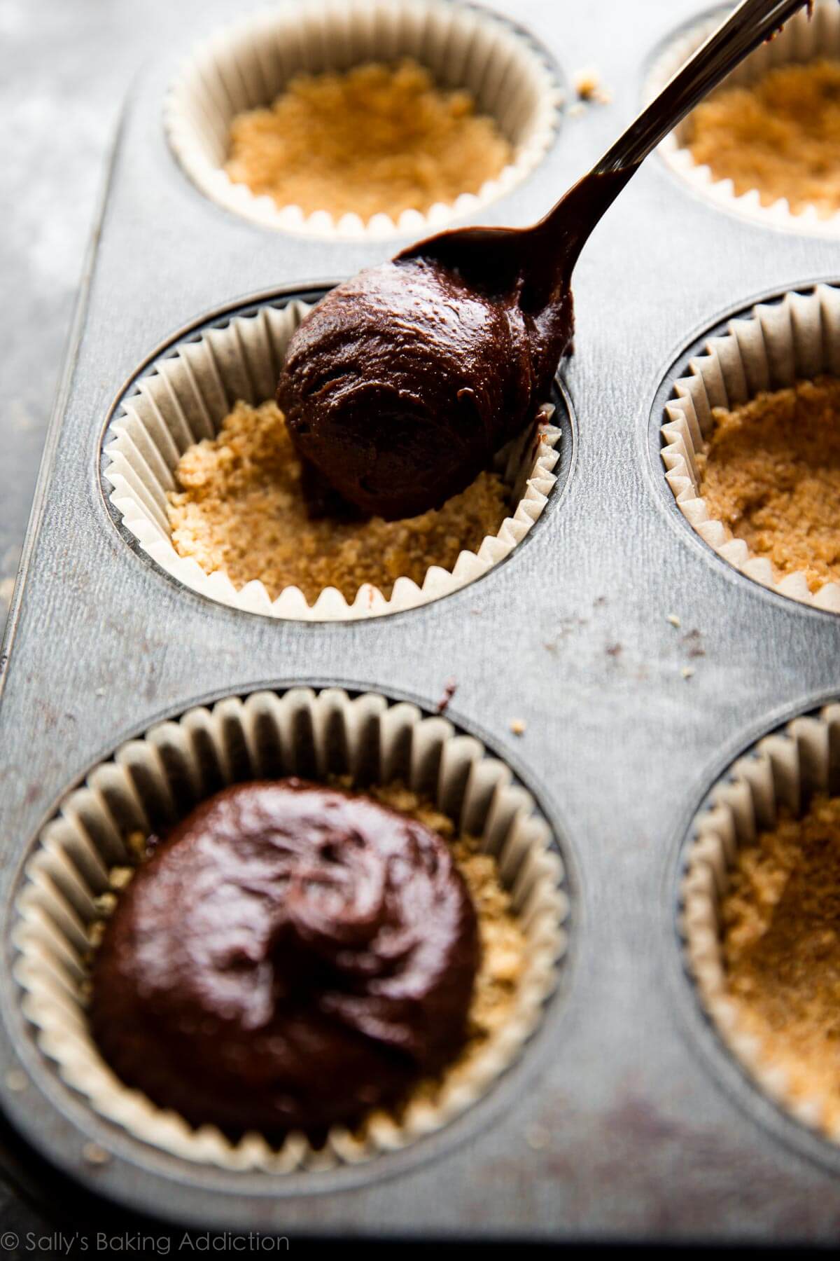 spooning brownie batter onto graham cracker crusts in a cupcake pan