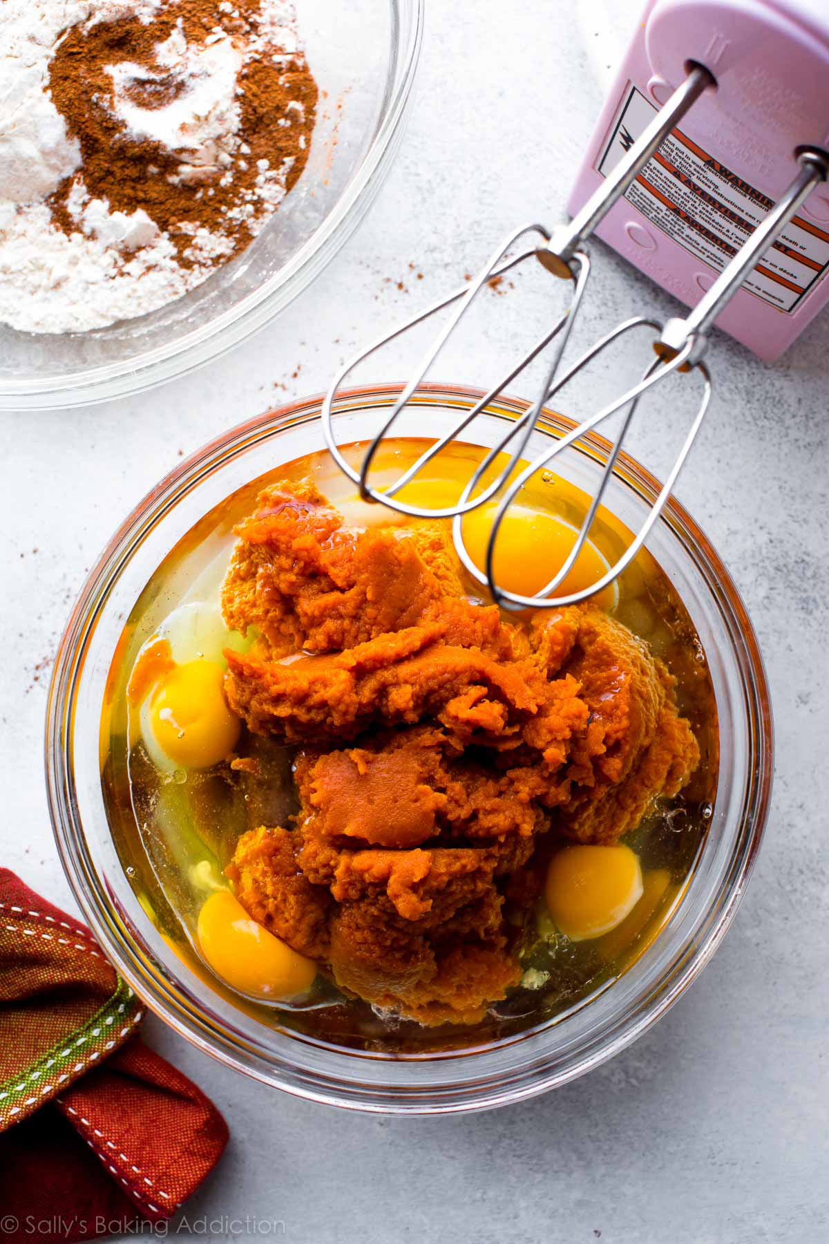 wet ingredients for pumpkin cake batter in a glass bowl with a pink hand mixer