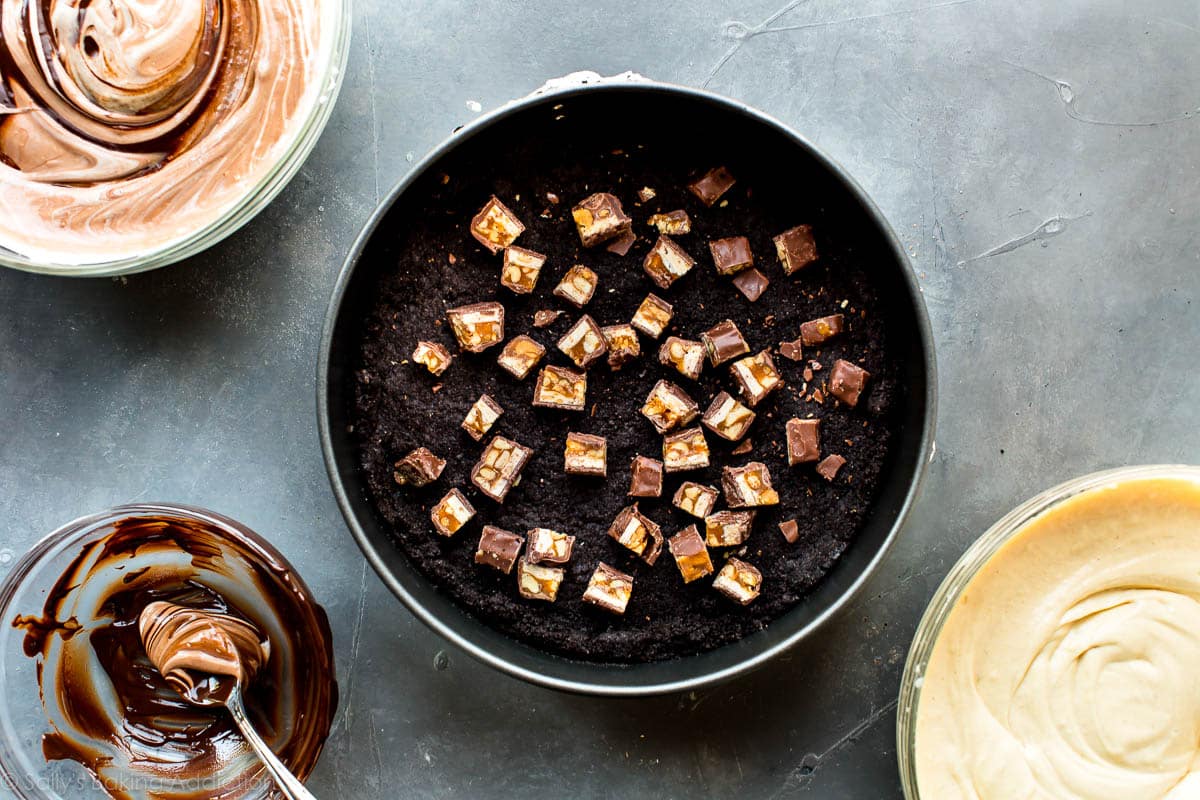 chopped Snickers on top of an Oreo cookie crust in a springform pan