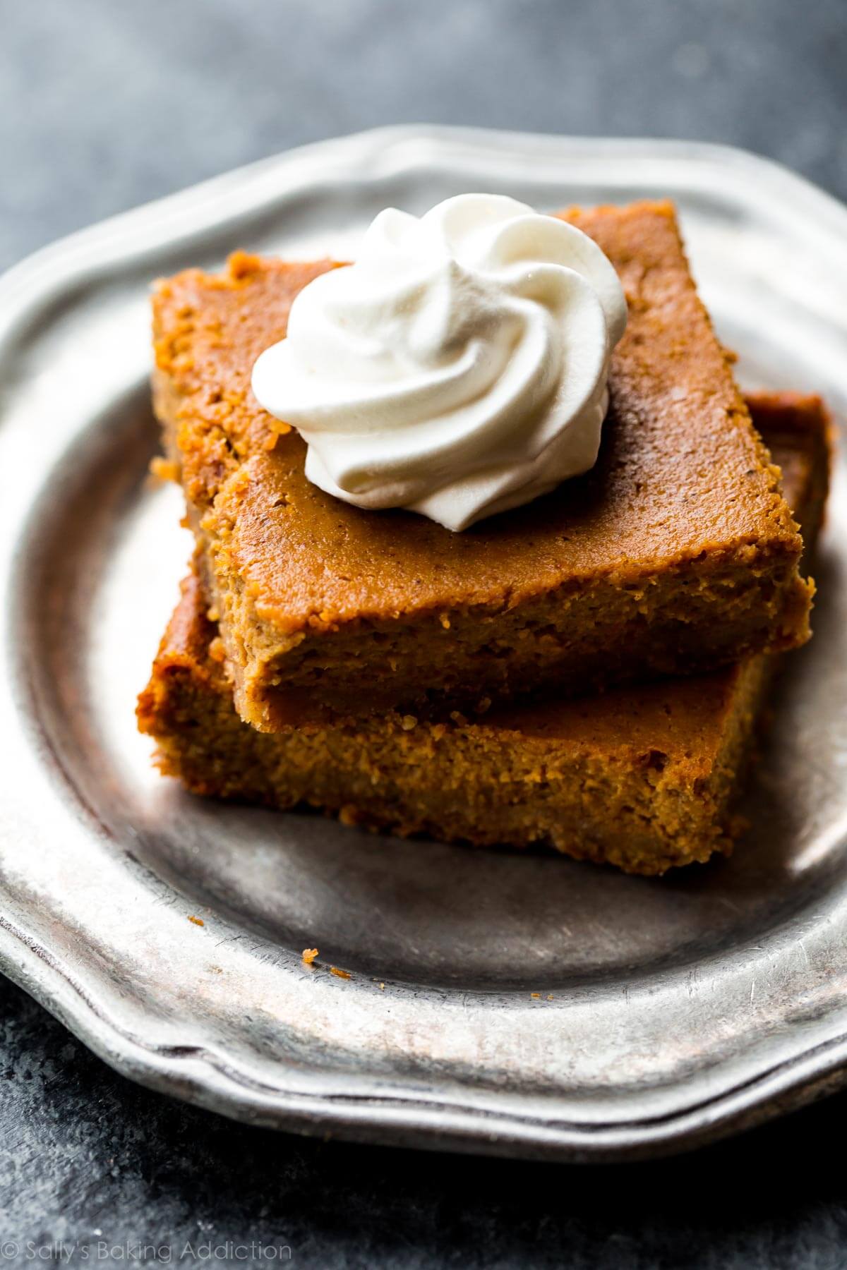 stack of 2 pumpkin pie bars on a silver plate with whipped cream topping