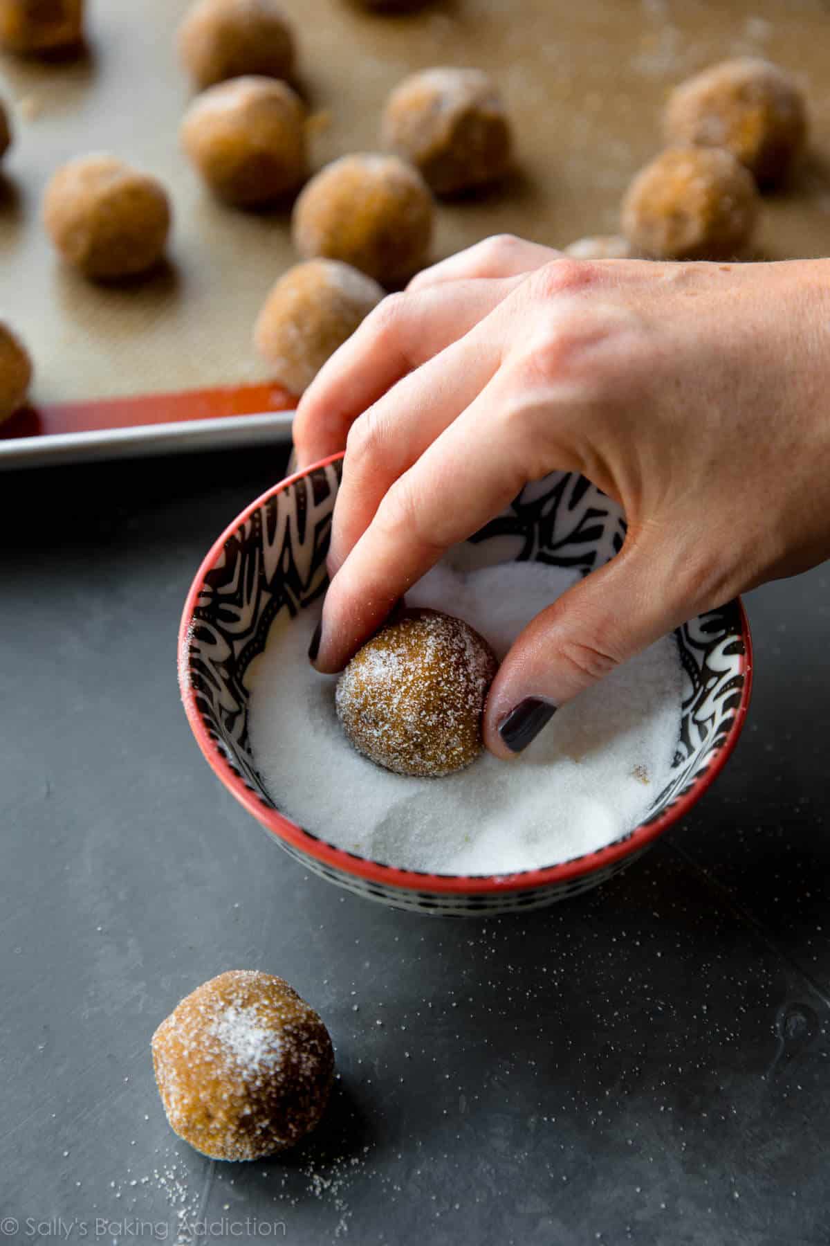 rolling a molasses cookie dough ball into a bowl of granulated sugar