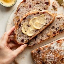 hand grabbing slice of buttered cranberry nut bread.