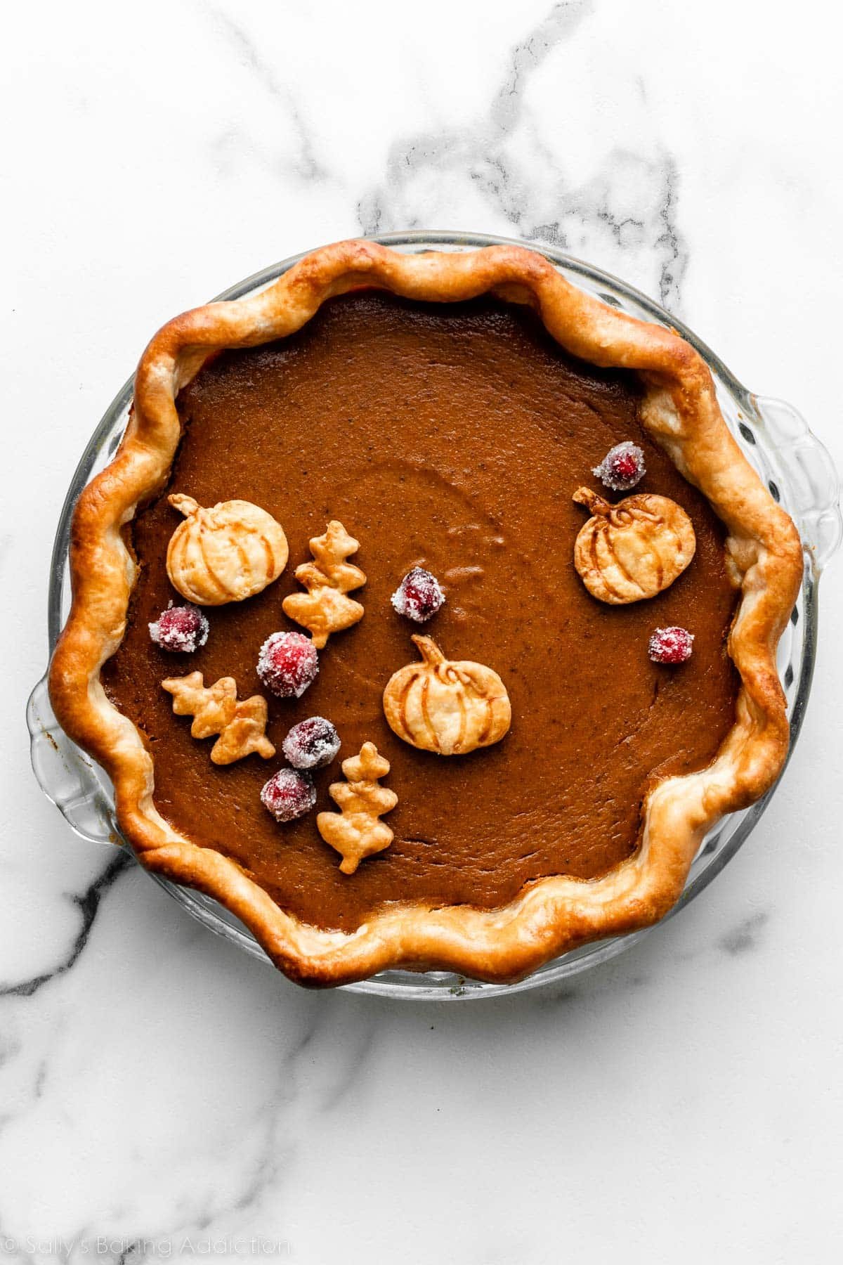 pumpkin pie with sugared cranberries and 6 leaf and pumpkin cookie cutter pie crust shapes on top.