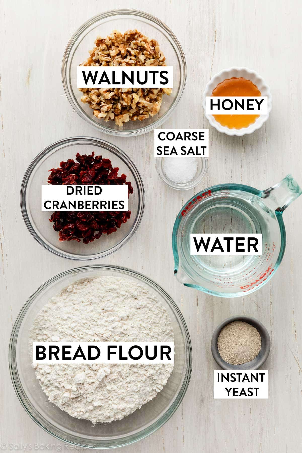 ingredients on wooden surface including flour, water, honey, salt, walnuts, and yeast.