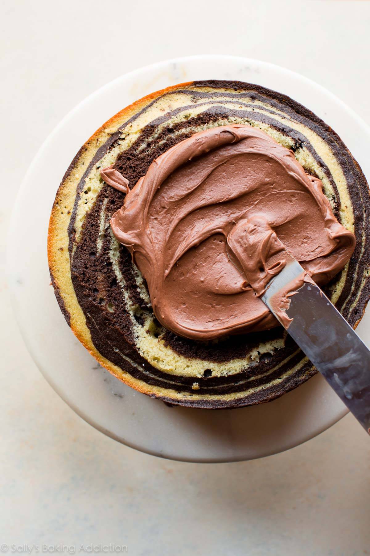 spreading chocolate cream cheese frosting onto layer of zebra cake