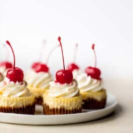 mini cheesecakes with whipped cream and cherries on top on a white plate