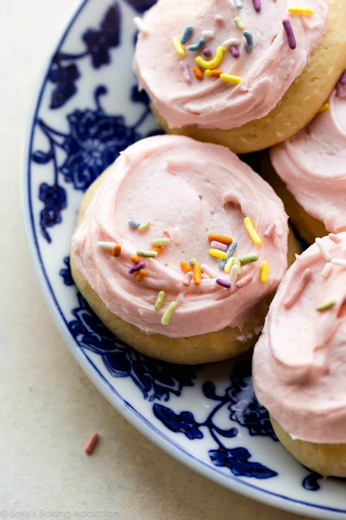 soft sugar cookies with pink buttercream and sprinkles on a blue and white plate