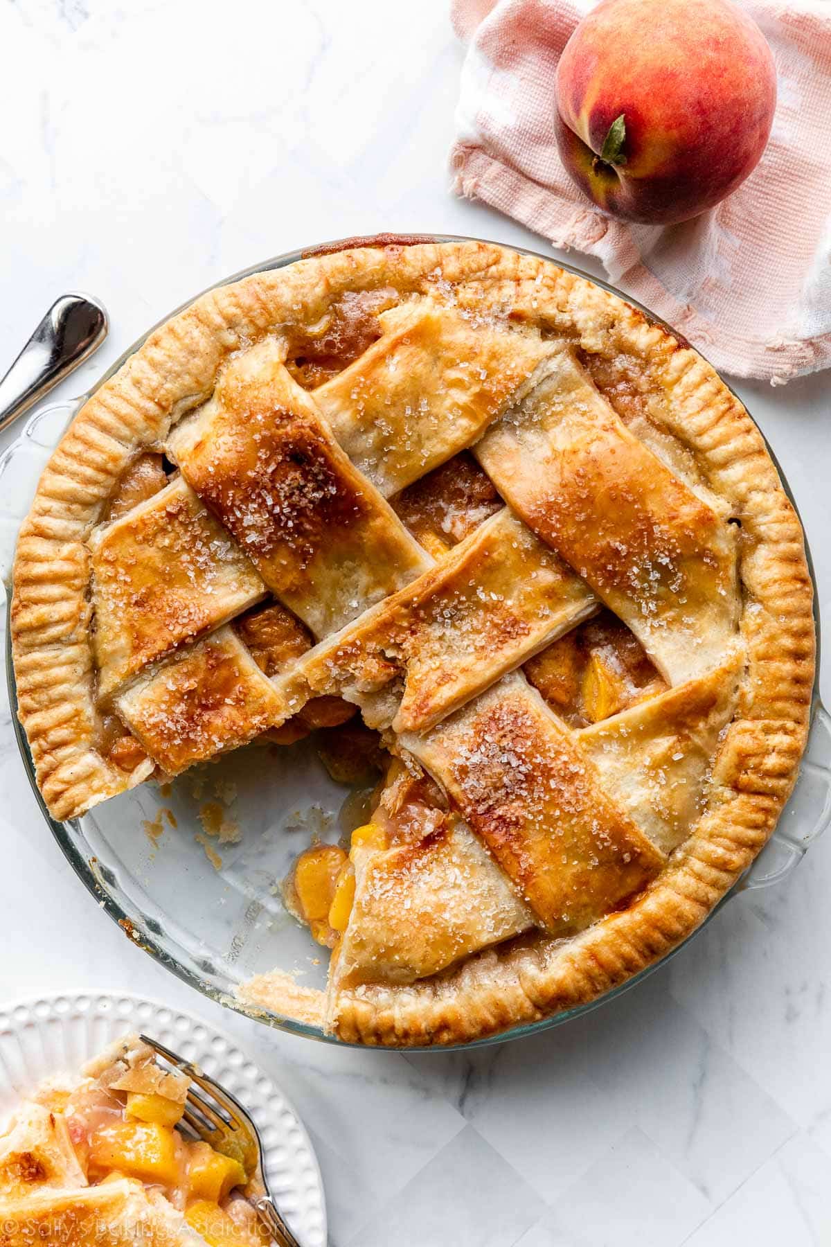 lattice peach pie in glass pie dish with slice taken out.