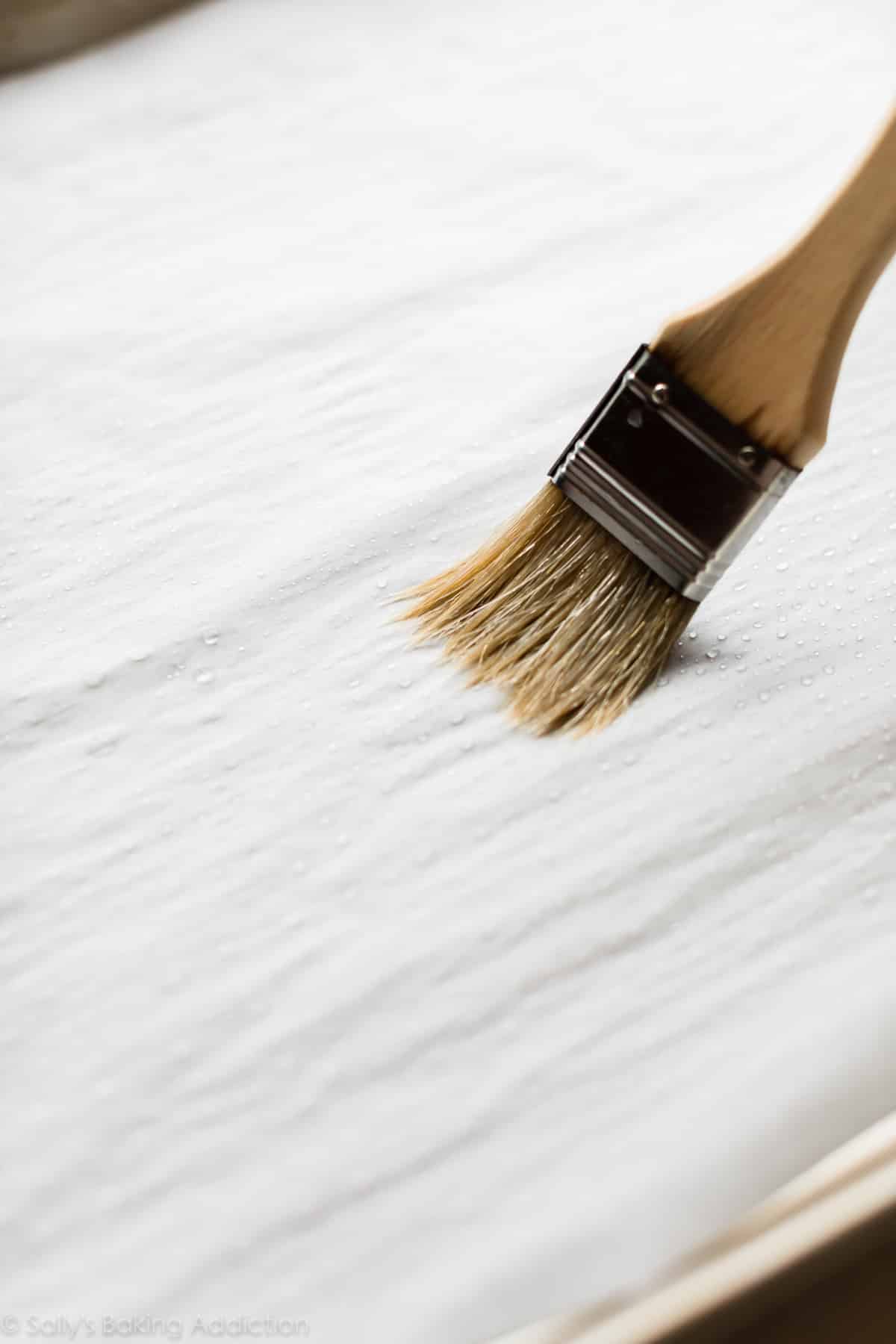 brushing water onto a baking sheet lined with parchment paper