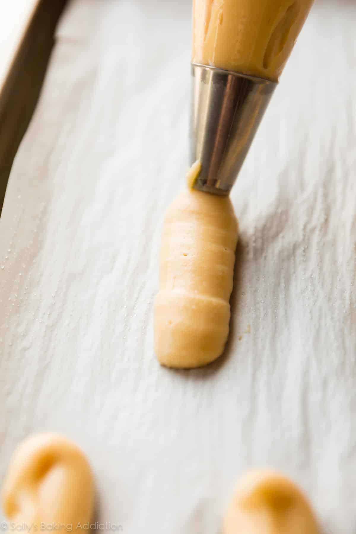 piping eclairs onto a parchment lined baking sheet