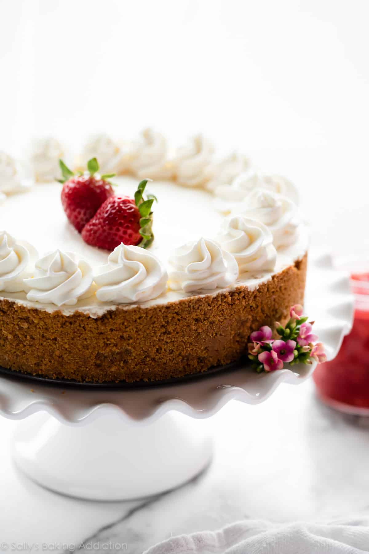 No bake cheesecake with whipped cream and strawberries on a white cake stand