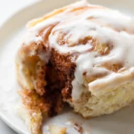 Cinnamon roll with vanilla icing on a white plate