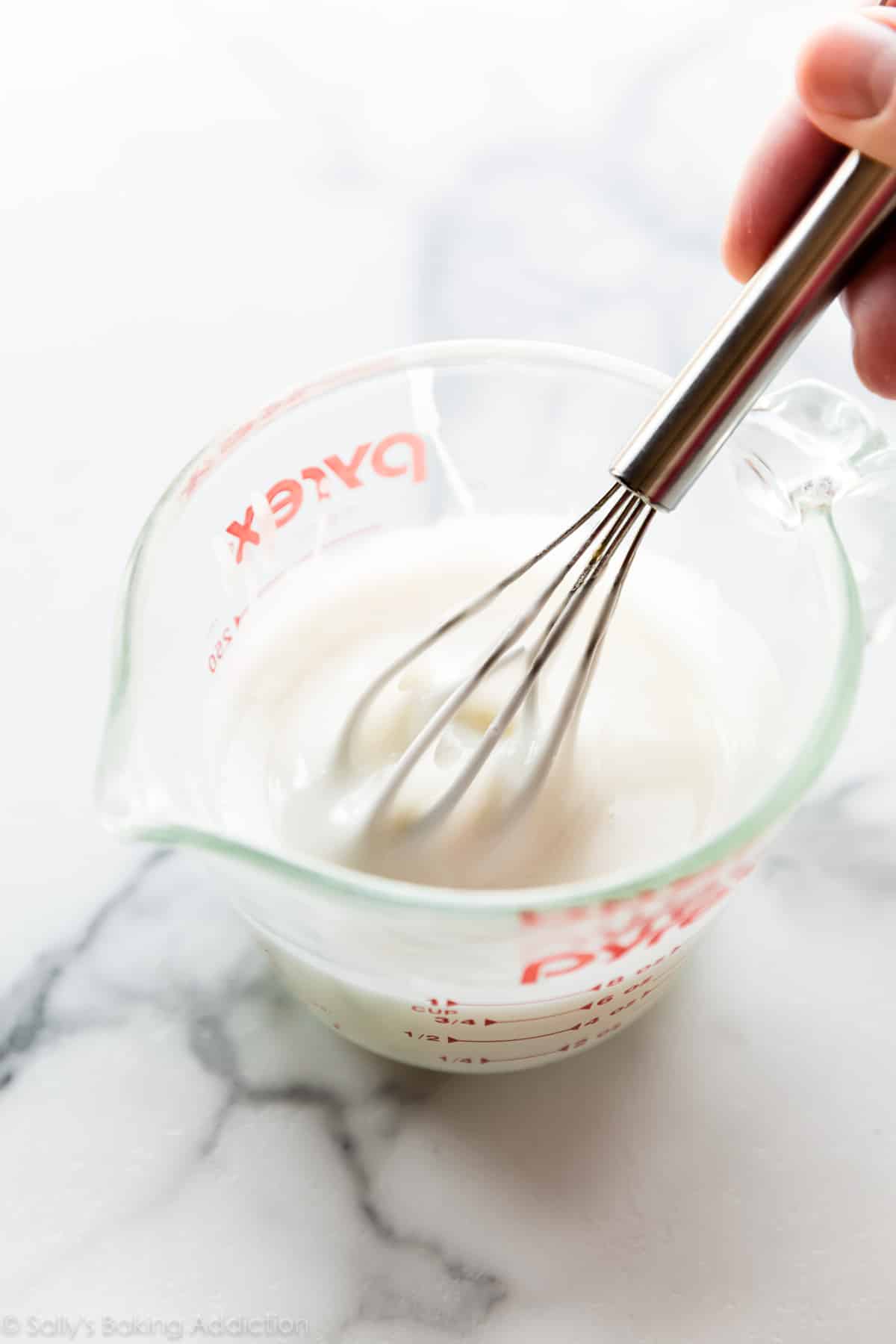 Whisking vanilla icing in a glass measuring cup