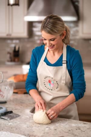 Sally wearing blue shirt and khaki branded apron working with dough on counter.