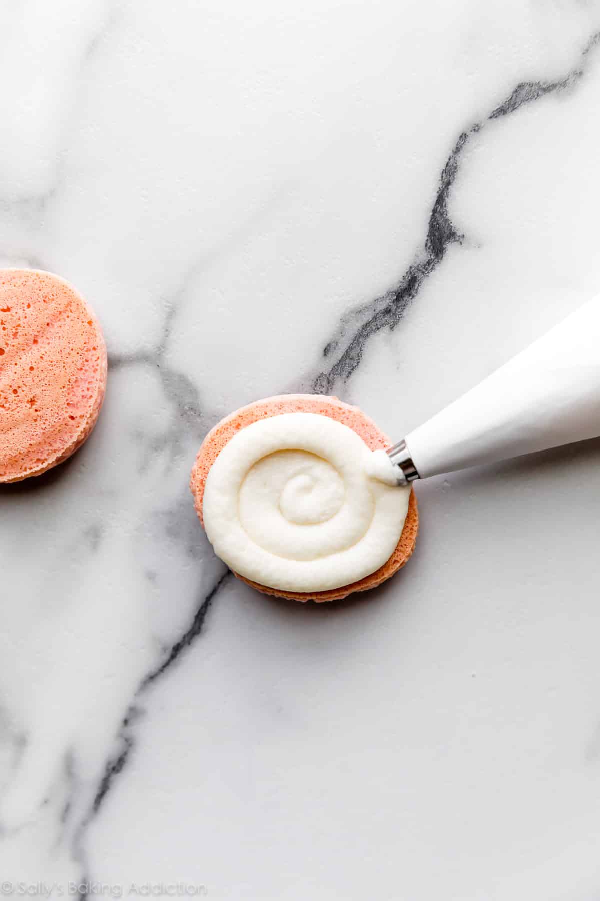 piping vanilla buttercream on a macaron shell