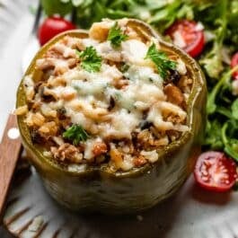 sausage stuffed green pepper on gray plate with arugula and tomato salad.