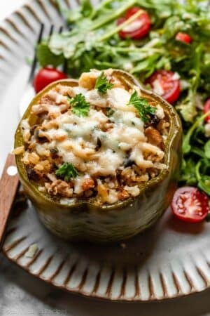 sausage stuffed green pepper on gray plate with arugula and tomato salad.