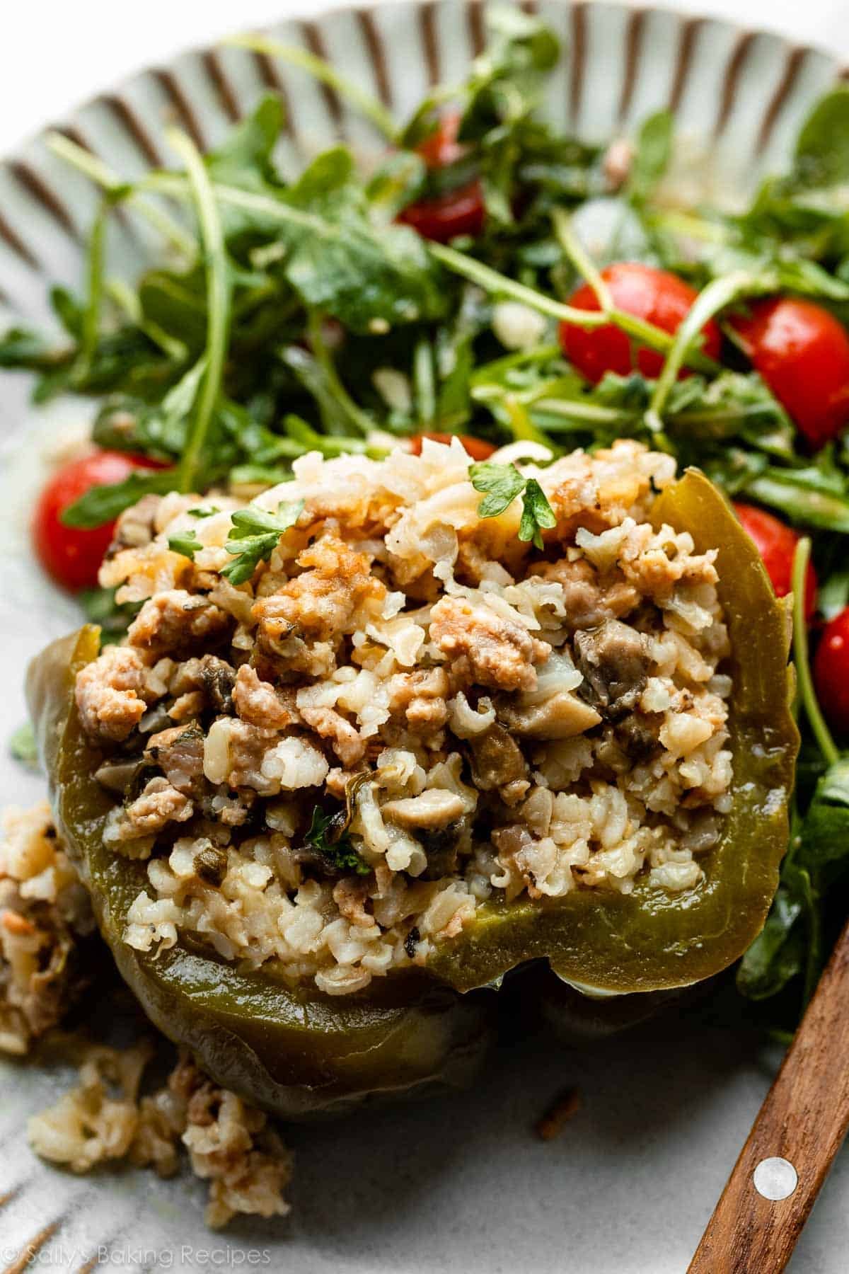 sausage stuffed green pepper sliced open on gray plate with arugula salad.