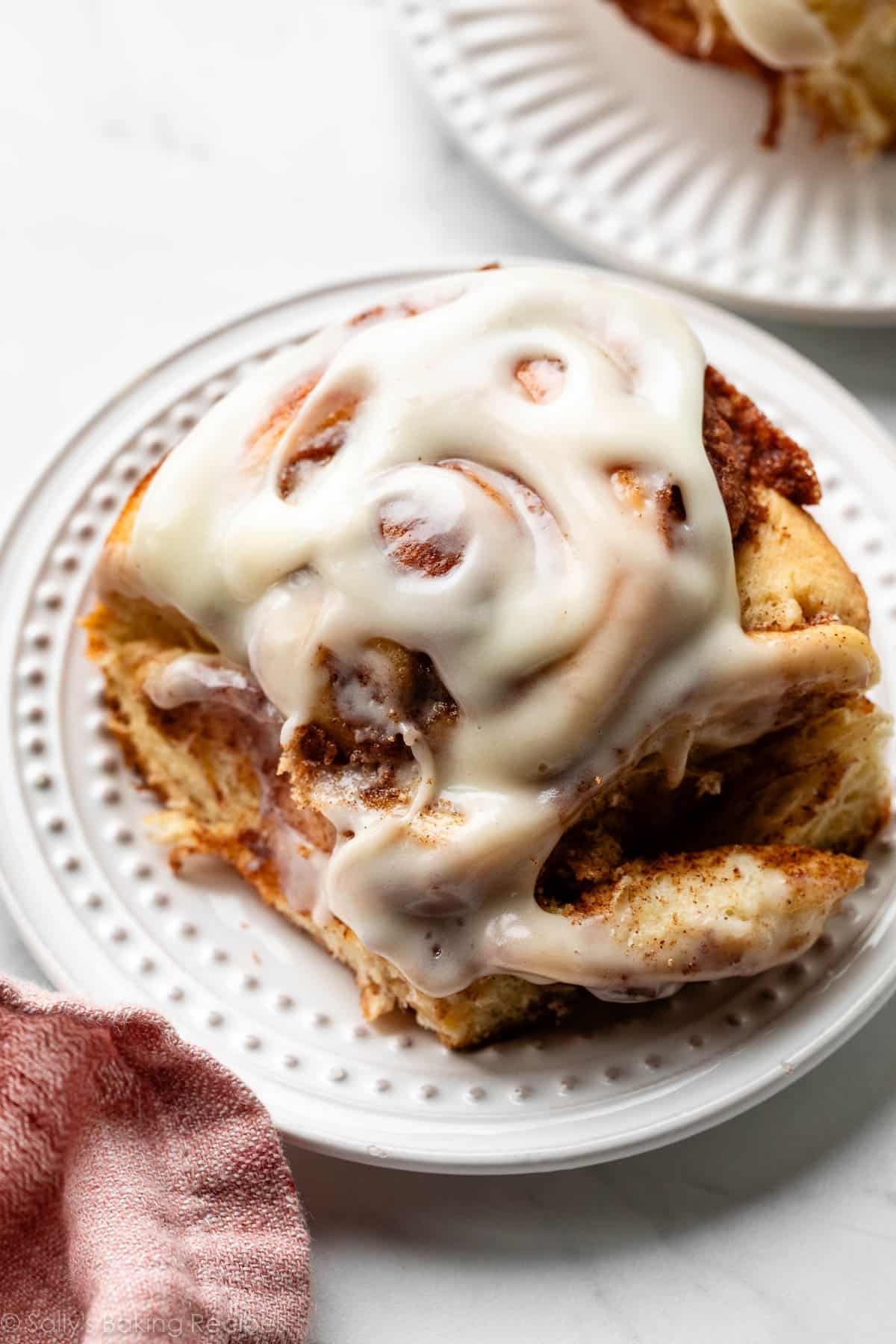 close-up photo of large cinnamon roll with cream cheese icing on white plate.