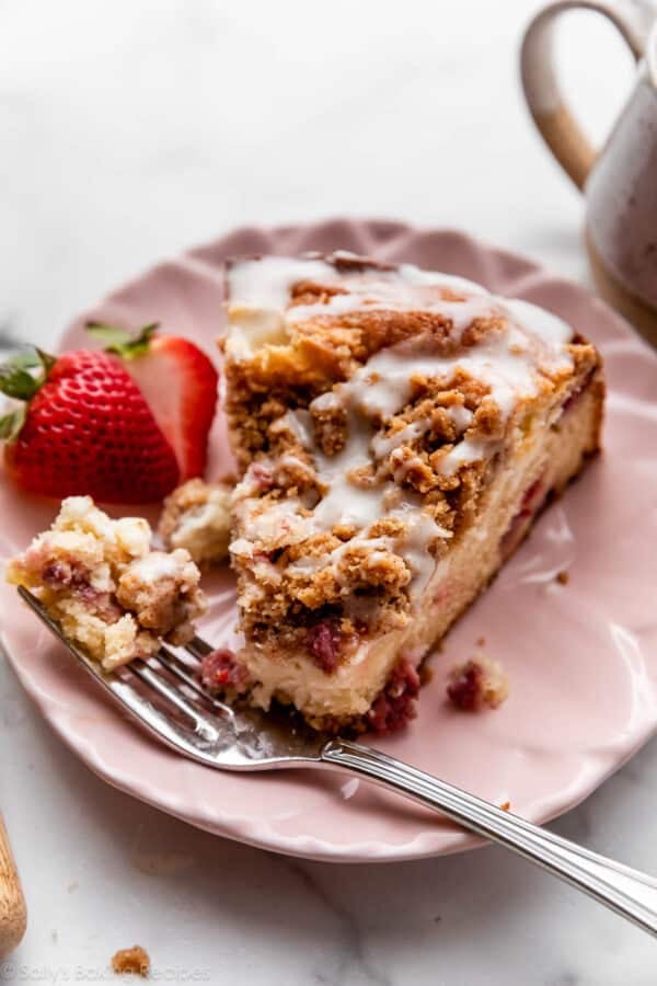 strawberry cream cheese crumb cake slice with crumb topping and icing on pink plate.