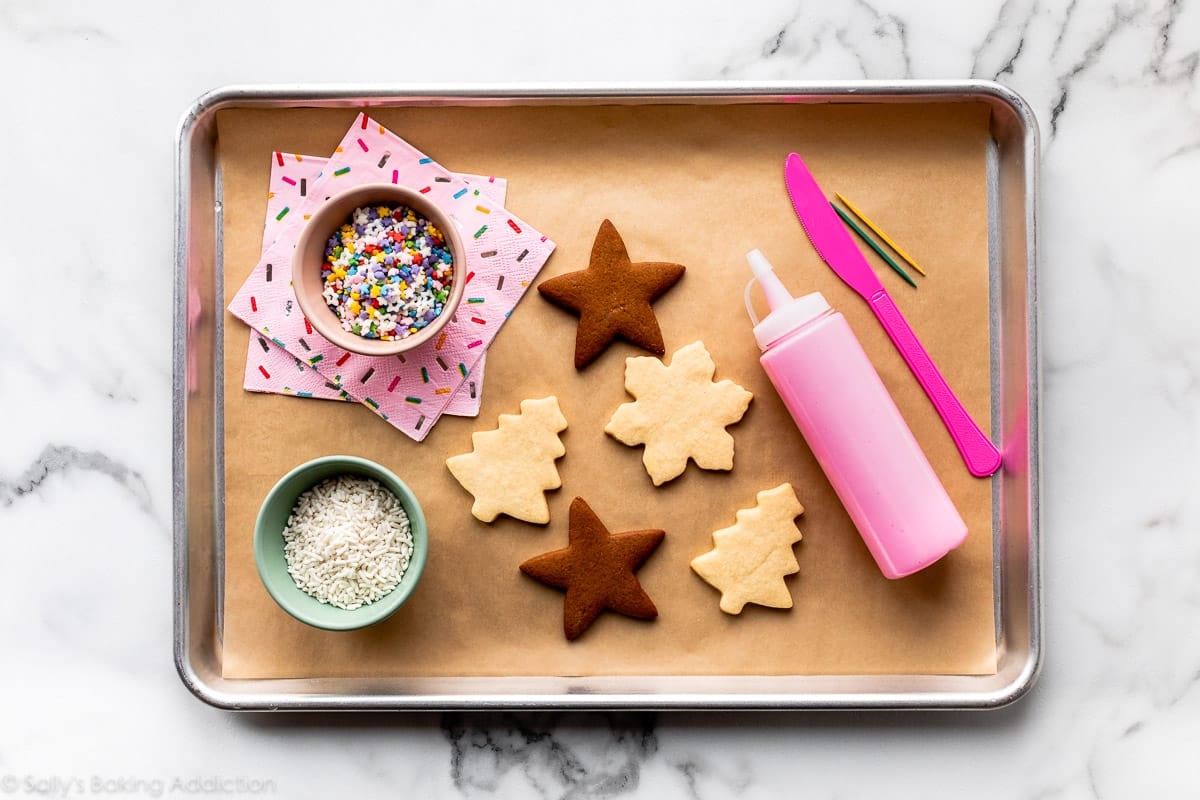 cookie decorating station with cookies, icing, and sprinkles on a lined baking sheet