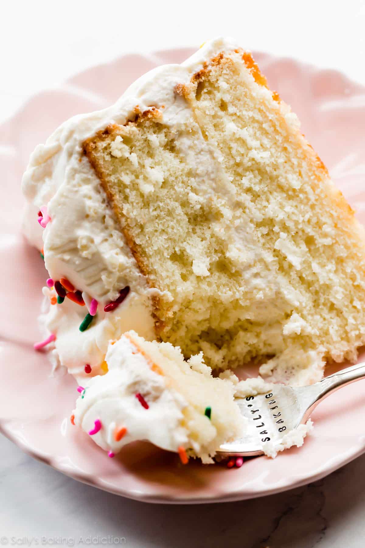 slice of white two layer cake with whipped frosting on pink plate