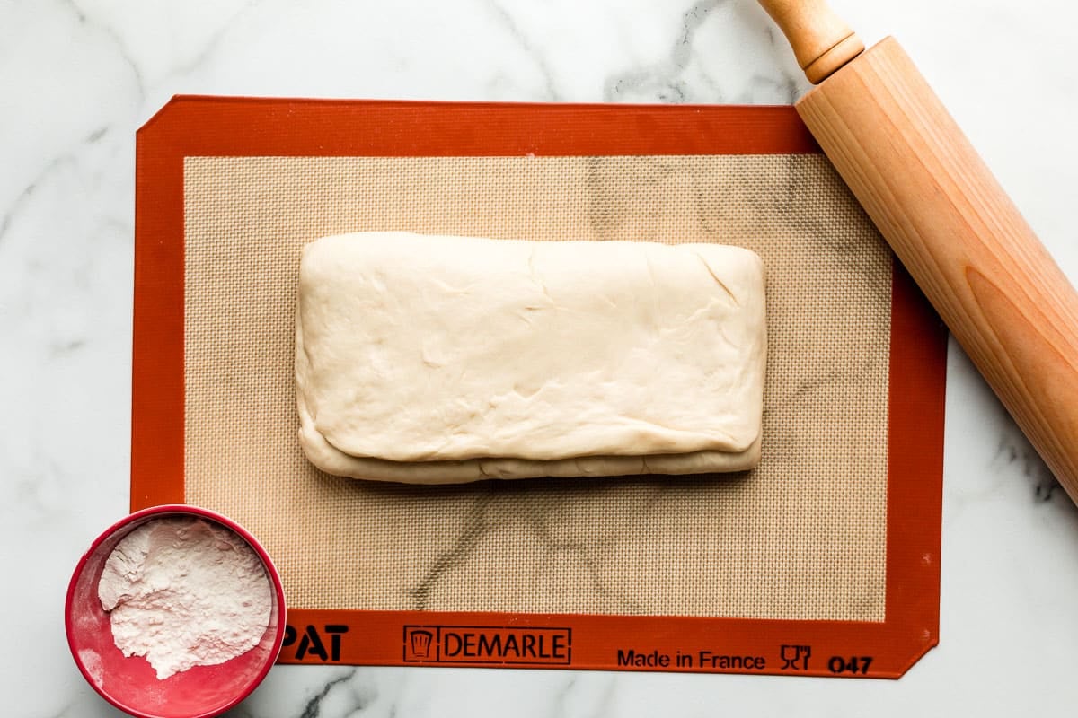 dough folded up on silicone baking mat lined baking sheet with rolling pin nearby