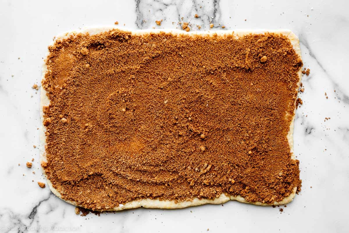 dough rolled out on marble counter with cinnamon and brown sugar on top.