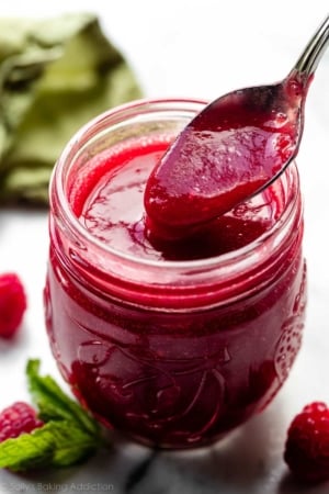 homemade raspberry dessert sauce in glass mason jar with spoonful being taken out.