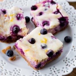 3 lemon blueberry cheesecake bars with graham cracker crust on white plate.