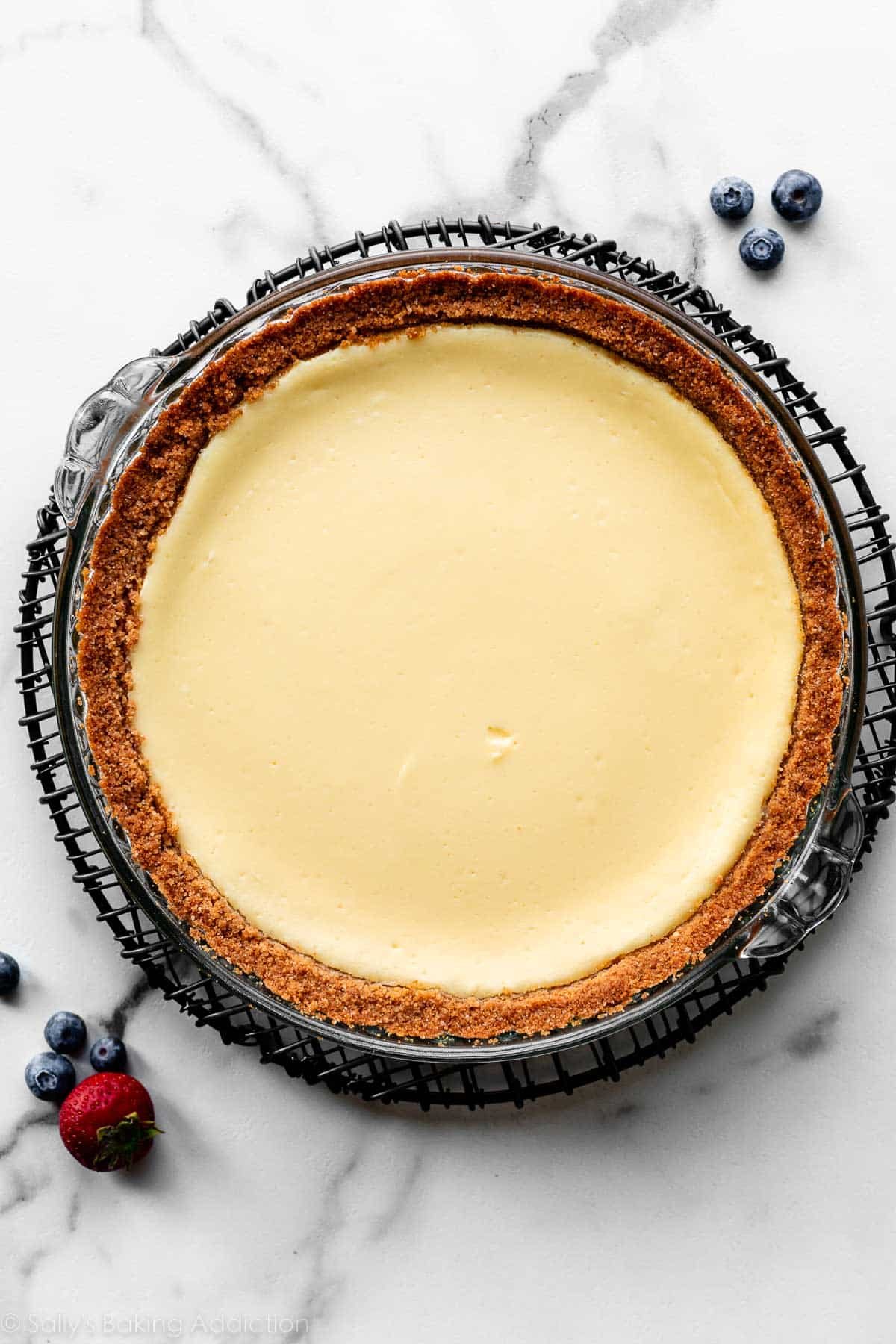 cooled cheesecake pie in glass dish on black circle wire rack.