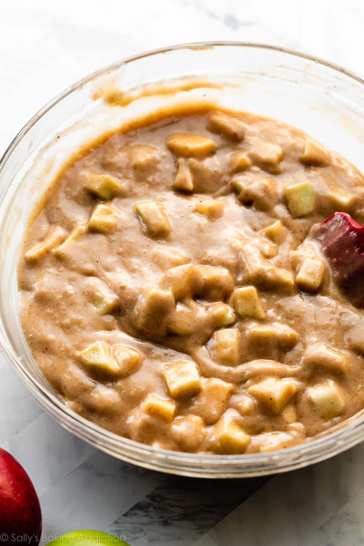 brown batter in glass bowl with apple chunks stirred in.