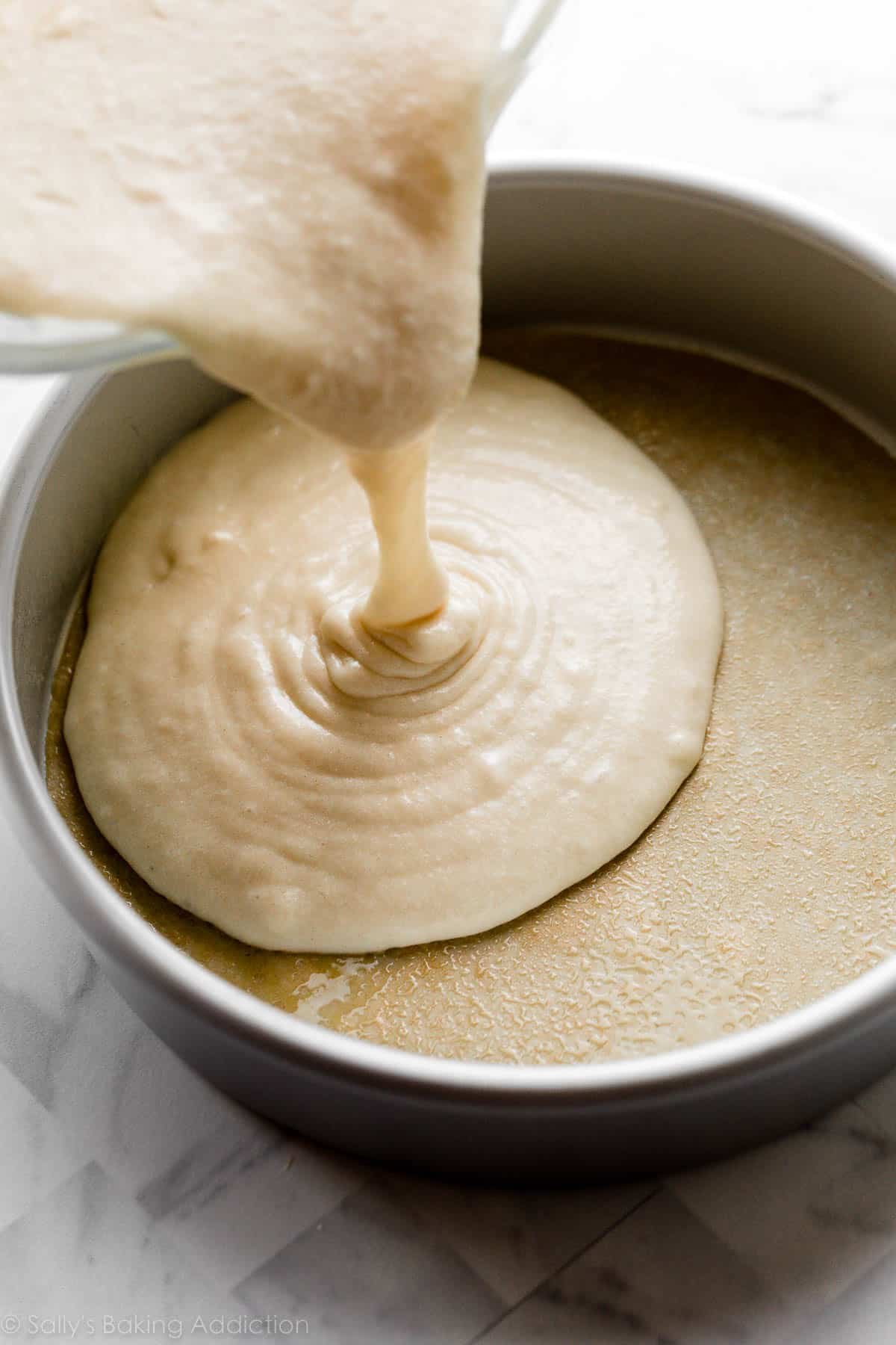 pouring batter in round cake pan lined with parchment paper round.