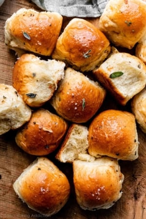 dinner rolls garnished with fresh chopped sage on wooden cutting board.